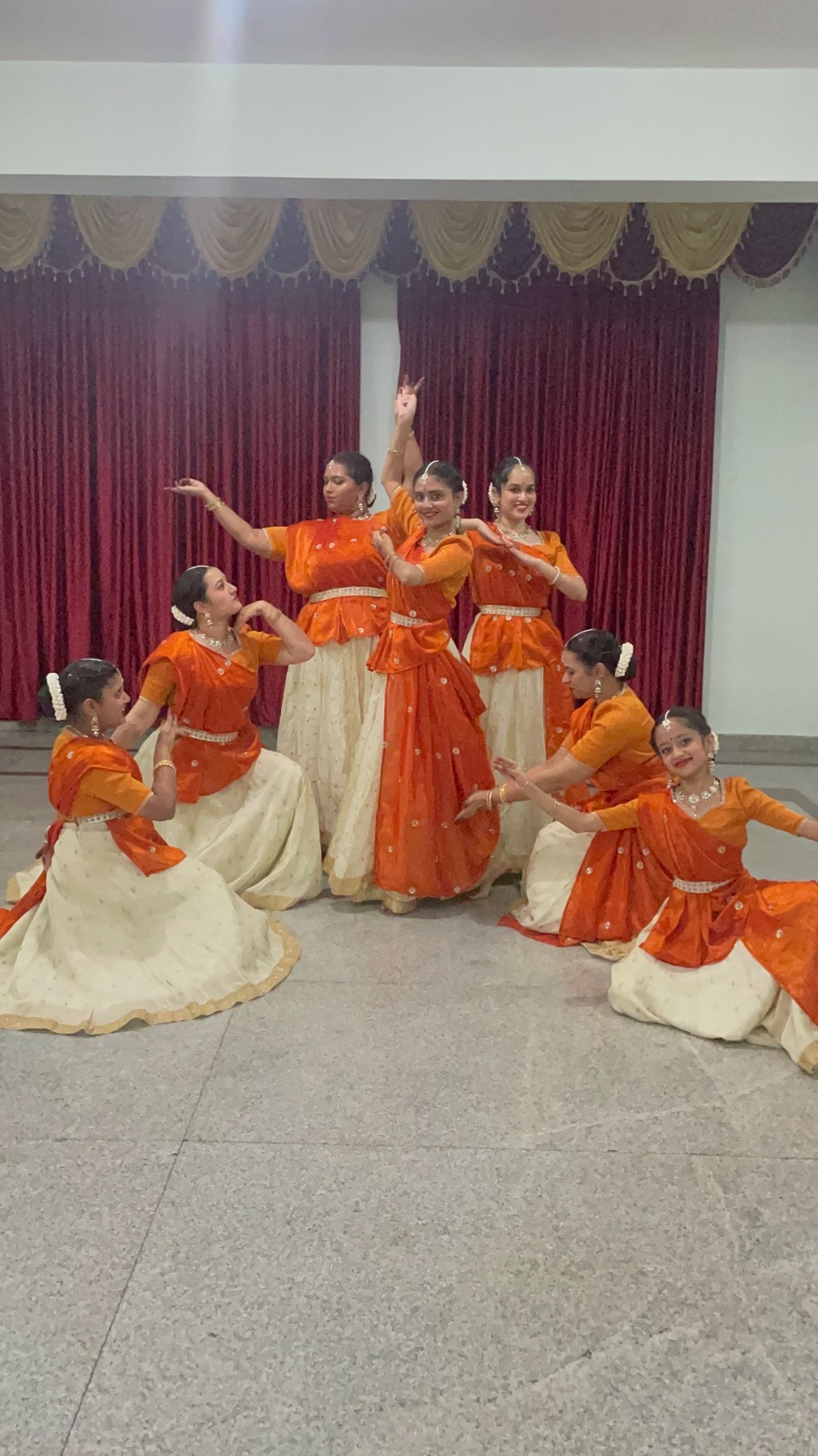 A group of Kathak performers in orange and white costumes.